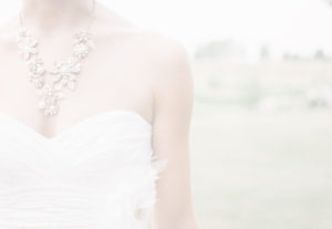 A close-up of a person in a strapless white dress and ornate necklace with pearls and floral designs, captured as if it were an oil painting. The background resembles a soft, blurred outdoor scene with green tones, evoking the timeless elegance of a Meissner masterpiece.