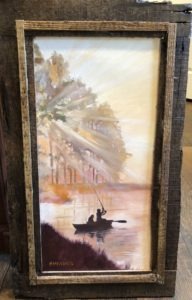 A framed painting captures the essence of morning fishing, with two people casting lines from a small boat on a serene lake. Sunlight filters through tall trees, creating golden reflections on the water. The rustic wood frame beautifully complements the warm and tranquil scene.