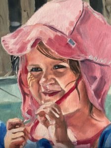 Painting of a child smiling and holding a red twig. The child is wearing a pink, wide-brimmed hat and has a small painted image on their cheek. The background is blurred and out of focus.