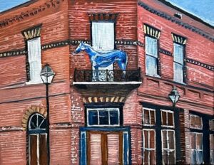Painting of a red brick building with a second-story balcony showcasing a blue horse sculpture. The structure has arched windows and doors, accented with brown and white detailing. Two street lamps line the sidewalk, setting the scene for vibrant local events.