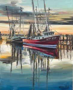 A red and white fishing boat is docked beside another boat at a wooden pier, reflecting in calm water. The sky is streaked with clouds and the colors of sunset. Tall masts and rigging rise above the boats.