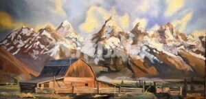 A rustic wooden barn stands in front of a fenced field, with tall, snow-capped mountain peaks rising dramatically in the background under a partly cloudy sky.