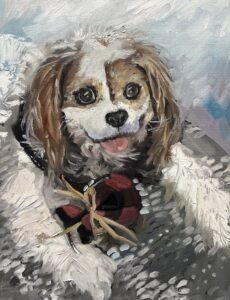 A painted dog with long ears and brown, white, and black fur lies on a blanket, holding a red and black ball tied with a yellow string. Its tongue is sticking out, and it looks up with a wide-eyed expression—capturing the charm that makes Custom Pet Portraits so treasured.